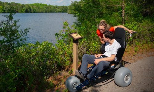 A man in an all-terrain wheelchair visiting Atsion Recreation Area with a companion.